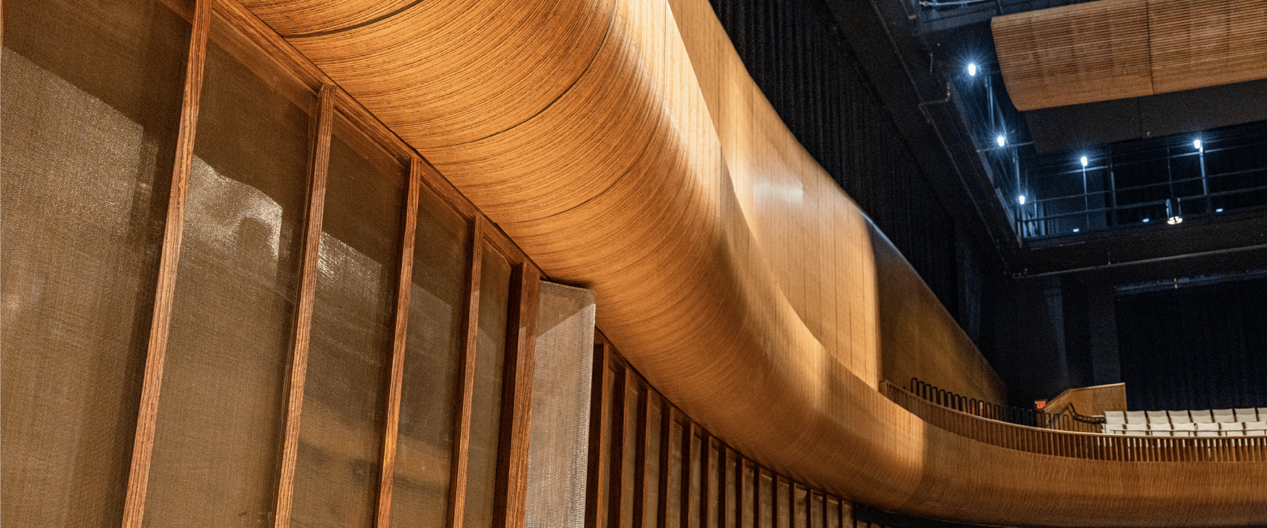 Curved flexible panels in a music hall, finished in a warm wood veneer. 